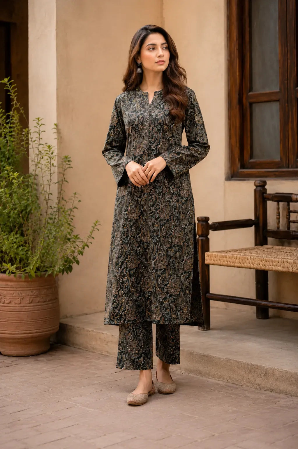 A woman wearing a long-sleeve kurta and matching pants in a dark olive green and black floral print.